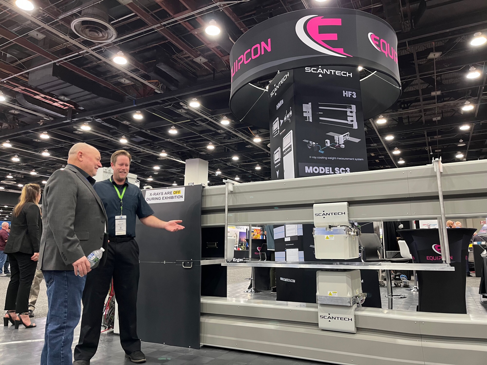 Matthew Baker of Gauge Advisor standing in front of manufacturing equipment at a trade show, specializing in process measurement and control